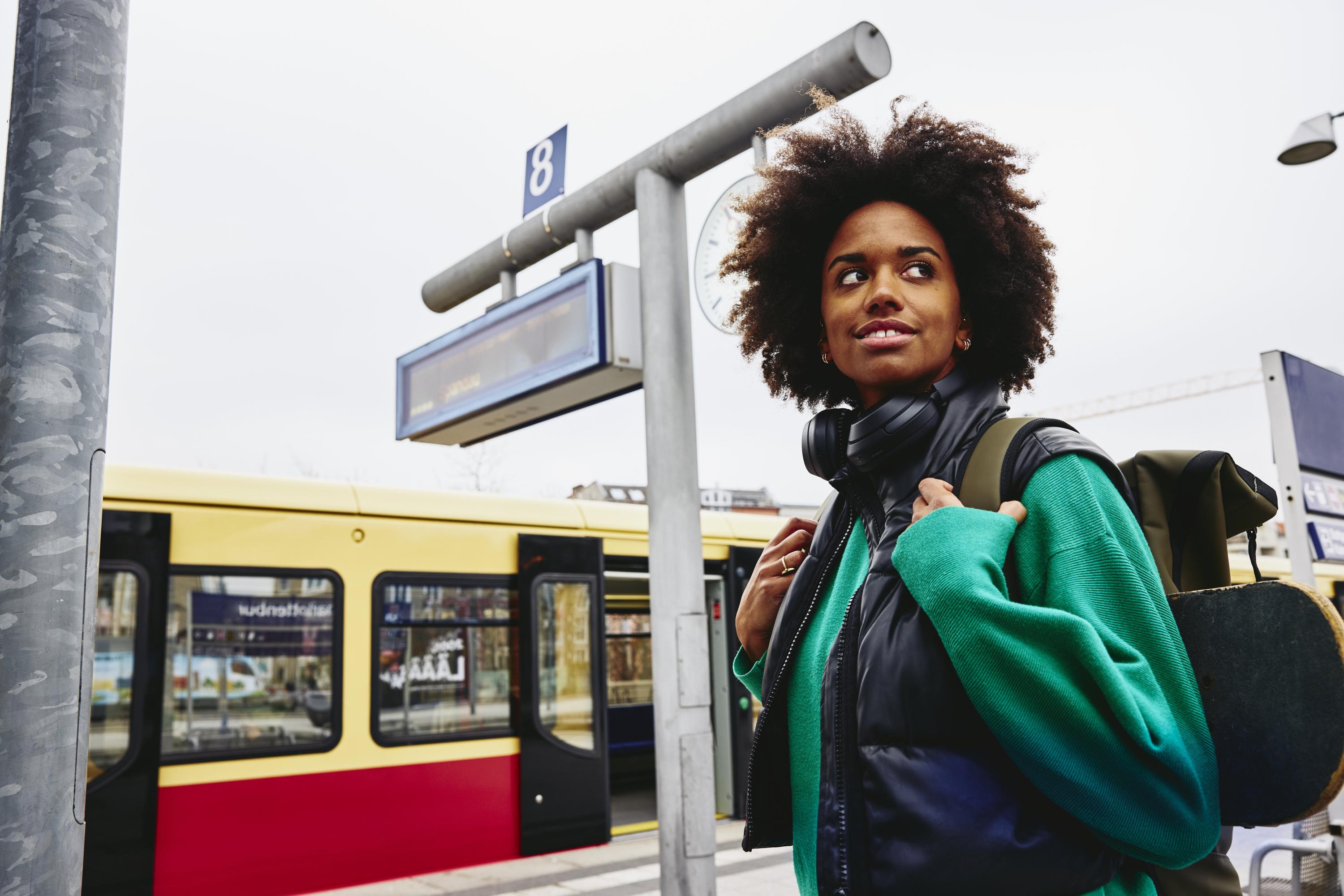 Smiling woman, looking away on train platform. Train in background.