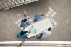 Arial view of nurses and one doctor pushing one patient in a bed in hospital corridor.