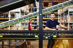 Smiling male standing behind a conveyor belt 

