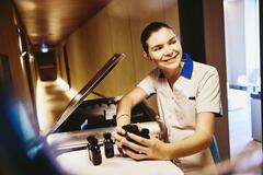 Woman in housekeeping uniform, holding small toiletries bottles.