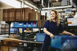 Smiling woman standing next to conveyer belt holding a crate