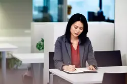 Womale sitting at a desk writing on a notebook.
