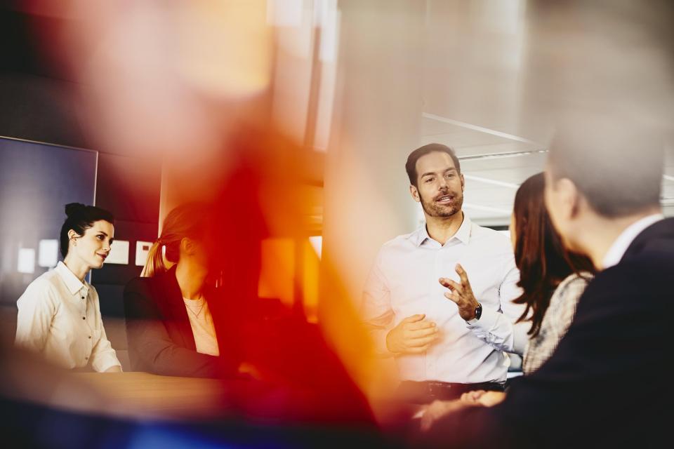 Business men and women in an office having a meeting. Primary color: red.