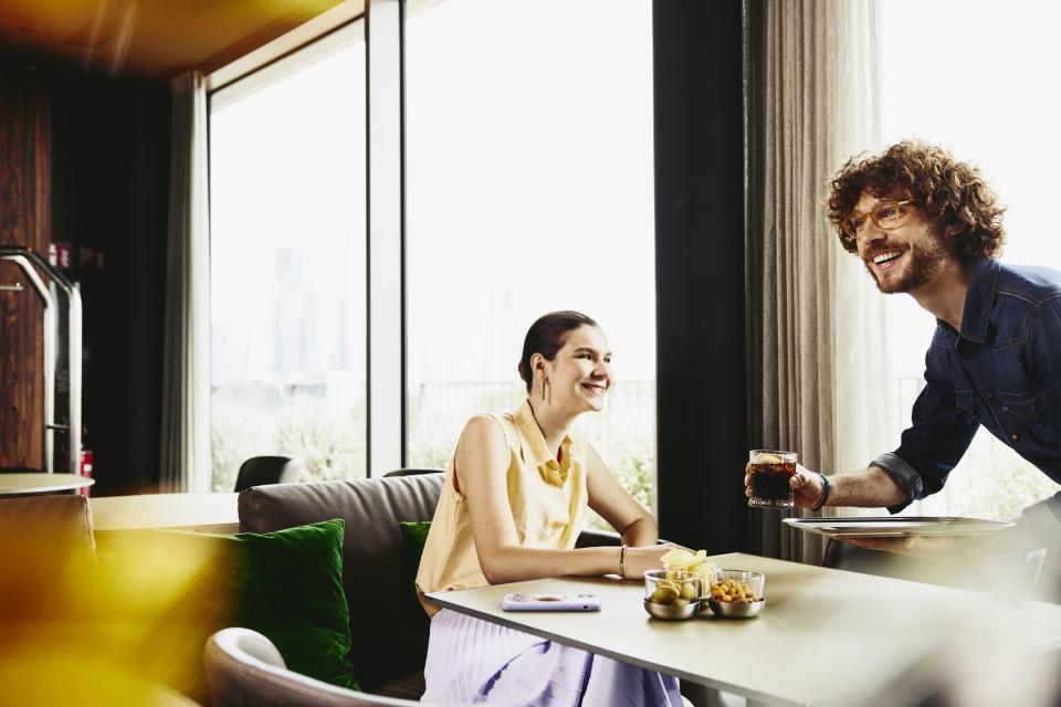 Waiter serving a drink to woman sitting at a table.