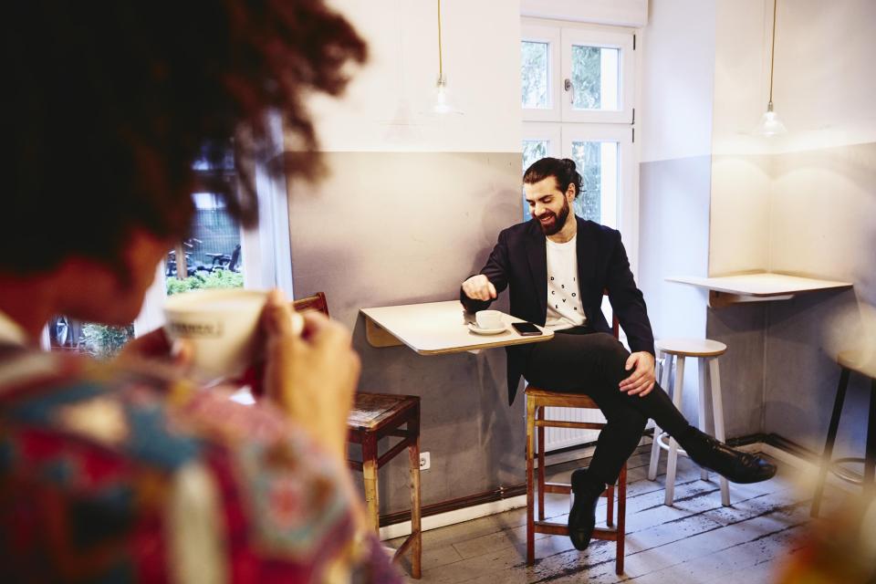 Man sitting at a table with coffee, looking down while having a conversation with someone.